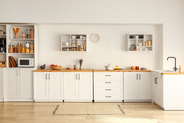 Interior of light modern kitchen with white counters, shelves and food - obrazy, fototapety, plakaty