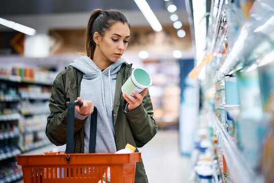 Young woman reads product label while buying diary product in supermarket.