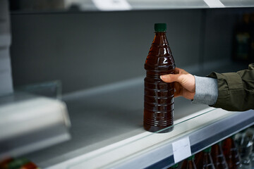 Close-up of customer takes the last bottle of cooking oil from supermarket shelf.