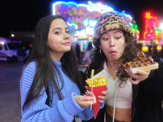 Woman hesitantly looking at a waffle next to a friend with fries in a night fair