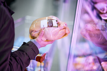 Close-up of woman buying chicken meat from refrigerated section at supermarket.