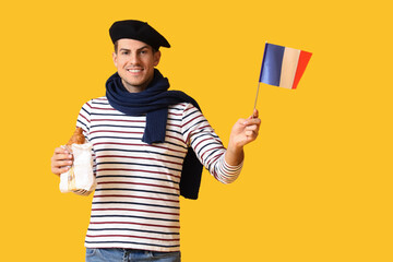 Handsome young man with flag of France and croissants on yellow background