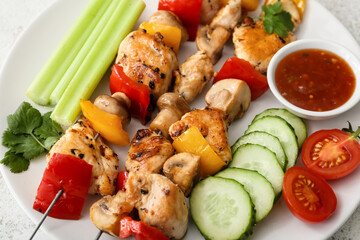Plate of grilled chicken skewers with vegetables and sauce on table, closeup