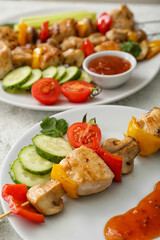Plates of grilled chicken skewers with vegetables on table