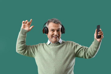 Senior man in headphones with mobile phone dancing on green background