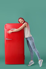 Beautiful young woman hugging red fridge on green background