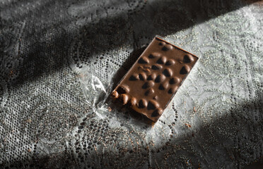 Single dark chocolate bar  on the table with hazel nuts and almond. Hard light. Organic handmade  black chocolate top view. Copy space. - obrazy, fototapety, plakaty