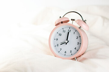 Morning concept. Classic pink alarm clock on the white wrinkled bed sheets close up image.