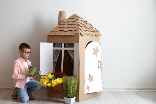 Funny little boy playing with cardboard house on light background