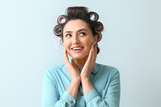 Beautiful young woman in hair rollers on light background - Powered by Adobe