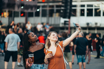 Friends taking selfie with a smartphone and drinking beer on a music festival