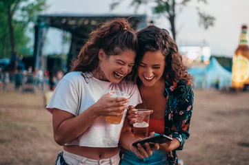 Poster Two beautiful friends using a smartphone on a music festival © Zamrznuti tonovi