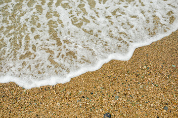 A small wave with foam rolls on the sea pebbles. Sea foam.