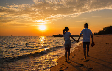 Silhouette of happy Asian couple hands holding and walking together on the beach while golden sunset time evening.