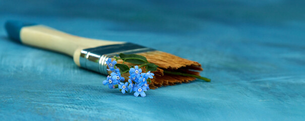 Obraz premium A painting flat brush with a branch of forget-me-nots in the bristles on a blue background. Copy space.