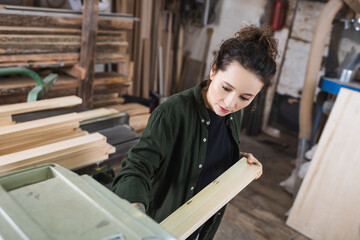 Fototapeta na wymiar Brunette carpenter holding wooden plank near thickness planer.