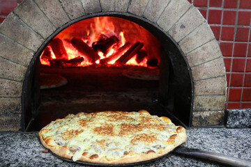 Piza na boca do forno a lenha com chamas acesas