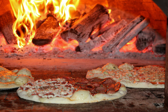 Três pizzas sendo assadas em ume um forno a lenha