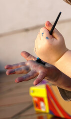 Mãos de uma criança que com um pincel pinta a palma de sua mão.