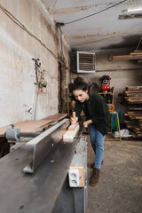 Fototapeta na wymiar Tattooed woodworker working with plank and jointer machine.