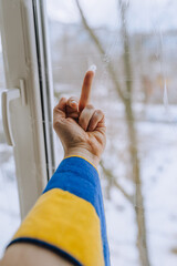 A Ukrainian man, being at home near a window in Ukraine under shelling in the war, shows an obscene gesture, the middle finger to the Russian occupiers. Concept, conflict, photography. - obrazy, fototapety, plakaty
