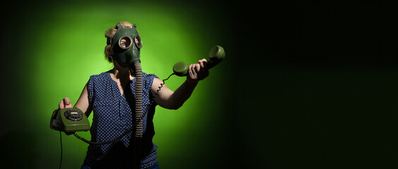 A woman in a gas mask passes the receiver of a retro phone on a dark dramatic background with copy...