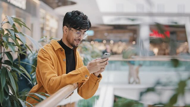 Happy smiling young arab guy stands with telephone in hands typing message on dating site chatting with friends using mobile application on smartphone writes sms checks email browses social networks