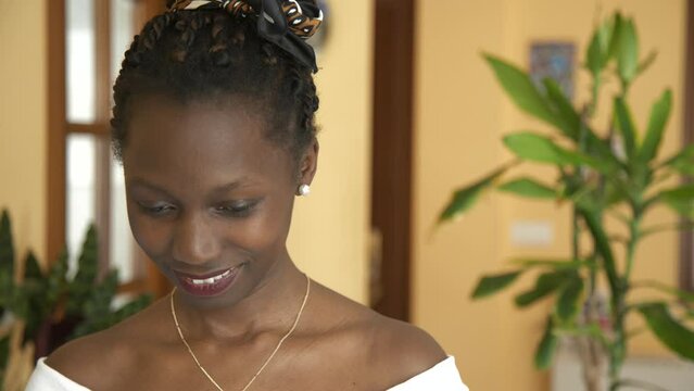 Beautiful young woman smiling looking at camera with white top and golden necklace,  living room with many green plants brackground
