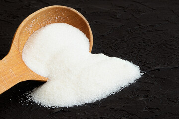 Scoop with powdered white sugar on a black background.Granulated sugar scattered on a dark...