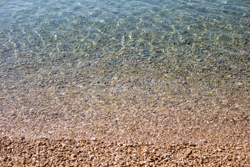 Texture of clean transparent sea water with pebble bottom. Pure water surface