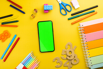 Green screen on the smartphone. Yellow background with school supplies, children's accessories, video game controller. Chroma Key - Powered by Adobe