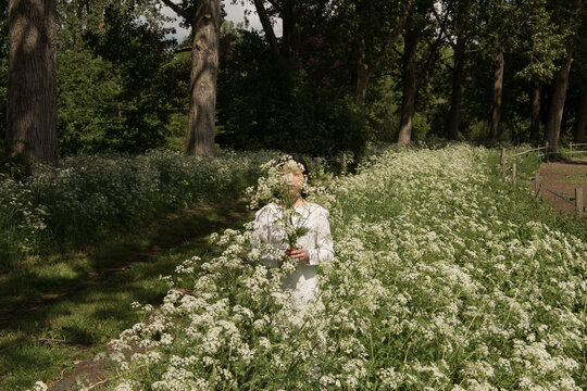 woman in white dress standing in green field of of wild cows parsly flowers in early spring