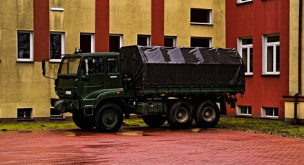 Wojskowa ciężarówka terenowa ( of road ) polskiej produkcji , Star 266 , z plandeką , w kolorze khaki , parkująca przed budynkiem , na powierzchni brukowanej kostką betonową , w strugach deszczu . - obrazy, fototapety, plakaty