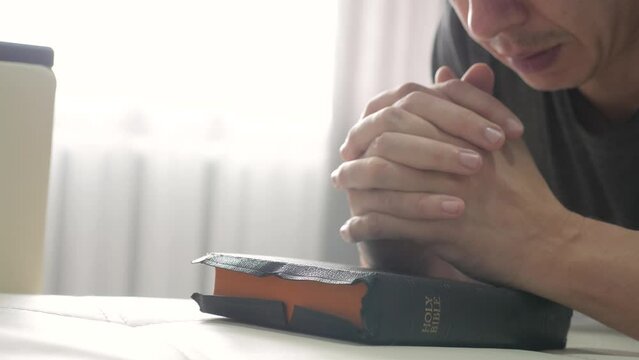 man praying indoors at bedtime on lifestyle bible. religion concept evening prayer human brunette hands on bible praying by bed