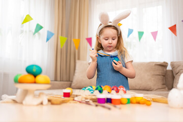 little girl with rabbit ears decorates Easter eggs with paints 