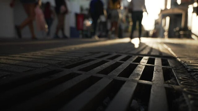 Close-up of the metal sidewalk slot drain on a pedestrian street at sunset. Urban drainage systems of the big cities