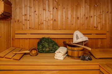 Wooden bucket with spoon, sauna hat, towels and broom on bench.