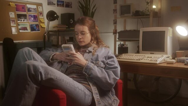 Young girl playing with a 90s portable game console in her bedroom.