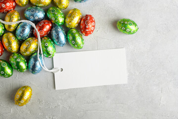 White rectangular Easter tag mockup with Happy Easter chocolate easter eggs on grey stone background. Easter label tag or sign for message greeting, favor tag, top view, flat lay