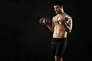 Fototapeta na wymiar Toning and defining his physique. Studio shot of a sporty young man working out with dumbbells isolated on black.