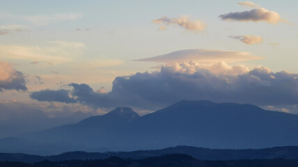 Fototapeta na wymiar Nuvole bianche sopra la cima dei monti al tramonto