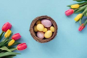 Happy Easter concept. Festive blue background with decorated eggs in nest and colorful tulips. Top view, flat lay, copy space