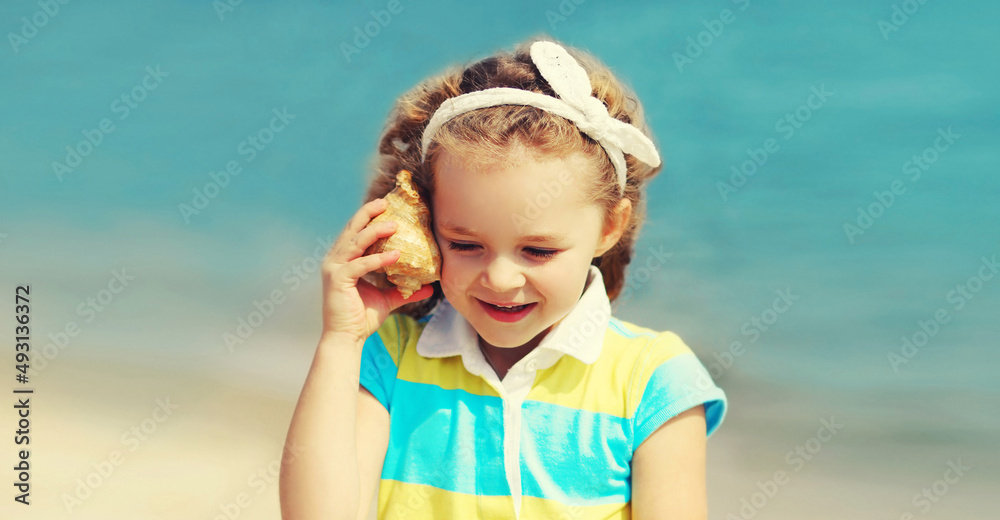 Wall mural Portrait little girl child puts a seashell to her ear to hear a sounds of the sea