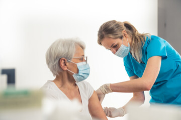 Young nurse working in a medical clinic helps out with vaccination process. Elderly people and vaccines concept. High quality photo - obrazy, fototapety, plakaty