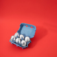 Creative Easter concept of cardboard box of eggs painted in silver aluminum foil. Pastel red...