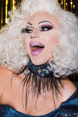excited drag queen with spectacular makeup and open mouth on shiny background.