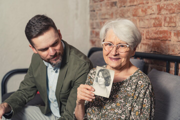 memories about youth presented by elderly content retired grandmother holding a photo of her in her...