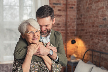 caucasian smartly dressed millennial man being affectionate with his elderly pensioner mother. High...