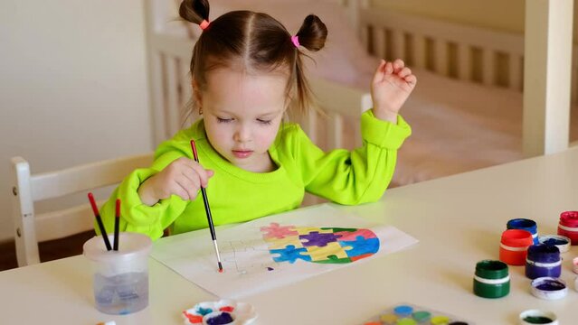 Little girl draws a heart with puzzles in watercolor and gouache on paper. Sweet baby is sitting at a table in the children's bedroom. Postcard for kids suffering from autism spectrum disorder