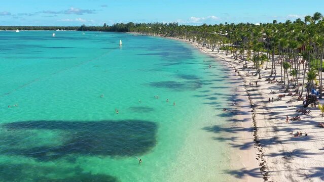 Tropical coastline with resorts, palm trees and caribbean sea with floating boats and people having fun doing paraseiling. Travel destinations. Dominican Republic. Aerial view